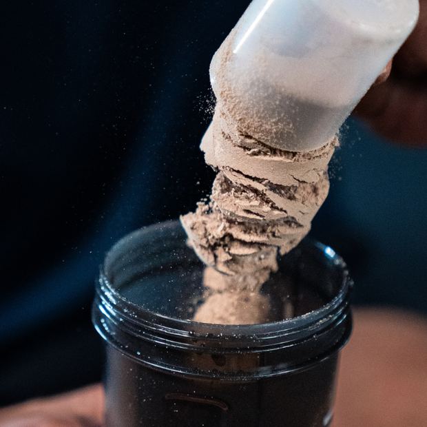 A scoop of chocolate protein powder pouring into a shaker