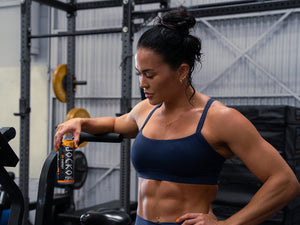 Athlete leaning on an assault bike in a gym, looking down at a Go Energy can in her hand