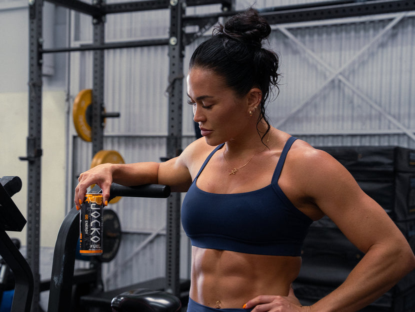 Athlete leaning on an assault bike in a gym, looking down at a Go Energy can in her hand