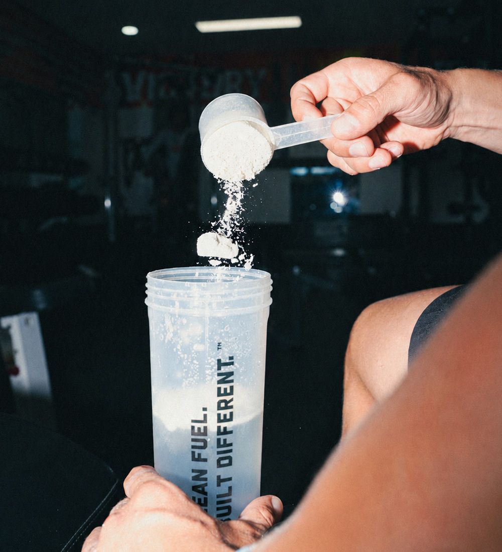 A scoop of protein powder pouring into the shaker
