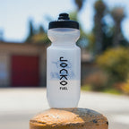 Clear water bottle with black lid and branding on a rock outdoors