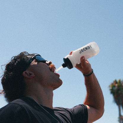 Person drinking from a Jocko water bottle against a clear blue sky