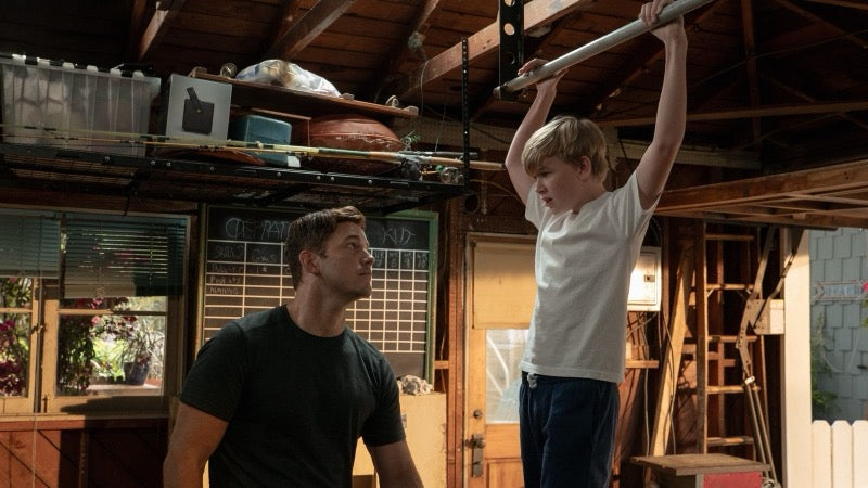 Chris Pratt as Uncle Jake coaching Marc through a pull-up under the Operation Warrior Kid board